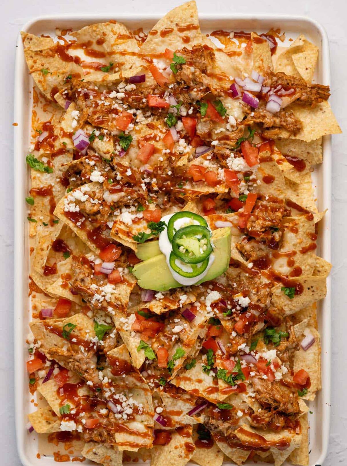 Oven-Baked Pulled Pork Nachos with Tomato, Cilantro, Red Onion, and Creamy Sour Drizzle